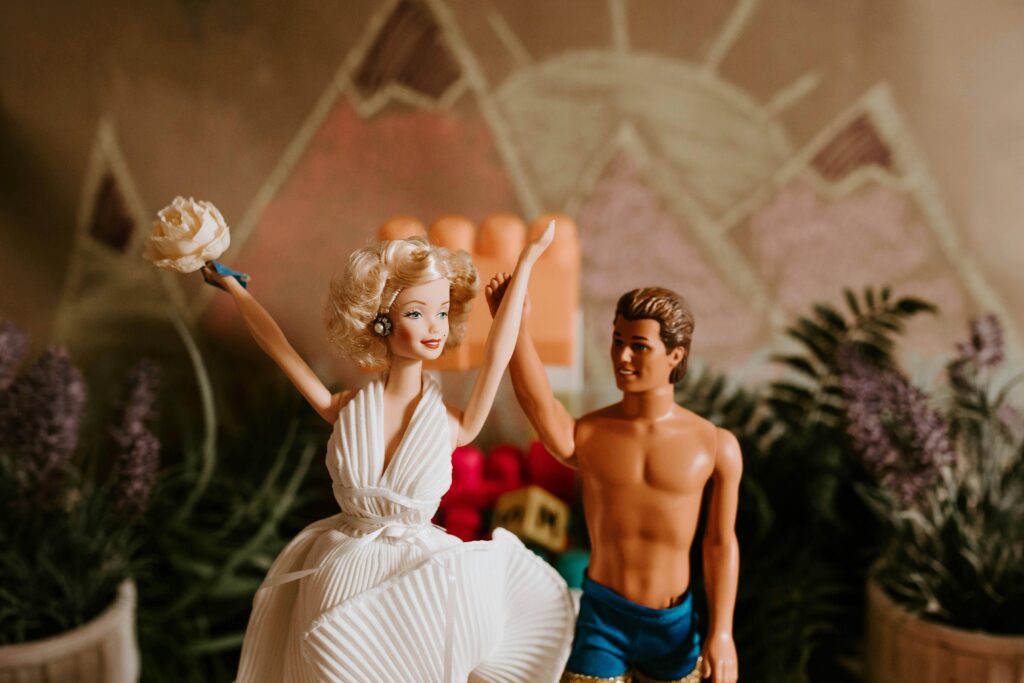 Two barbie dolls, hand in hand, positioned like they are getting married.